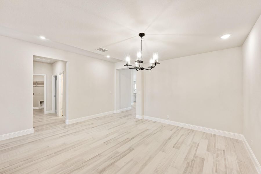 Empty dining room with light wood floors, white walls, and a black chandelier overhead Empty dining room with light wood floors, white walls, and a black chandelier overhead