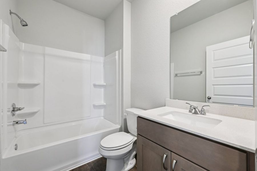 Image of a bathroom with brown cabinets, white countertops, a large mirror and a shower with a tub
