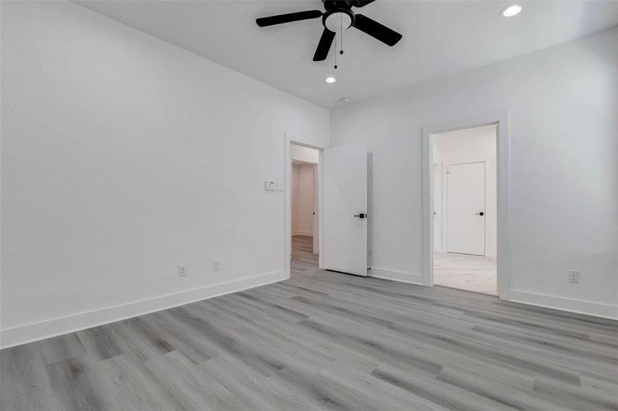 Spacious and serene, this bedroom features high ceilings, recessed lighting, a contemporary ceiling fan, and durable gray-toned plank flooring. Multiple doorways provide convenient access to adjoining spaces, while the clean neutral palette offers an inviting canvas for personalized furnishings and décor. Spacious and serene, this bedroom features high ceilings, recessed lighting, a contemporary ceiling fan, and durable gray-toned plank flooring. Multiple doorways provide convenient access to adjoining spaces, while the clean neutral palette offers an inviting canvas for personalized furnishings and décor.