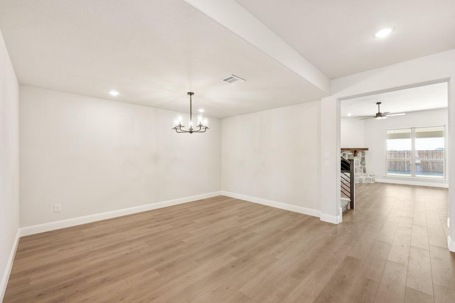 Empty dining room with chandelier, wood floors, and open view to living area with stone fireplace