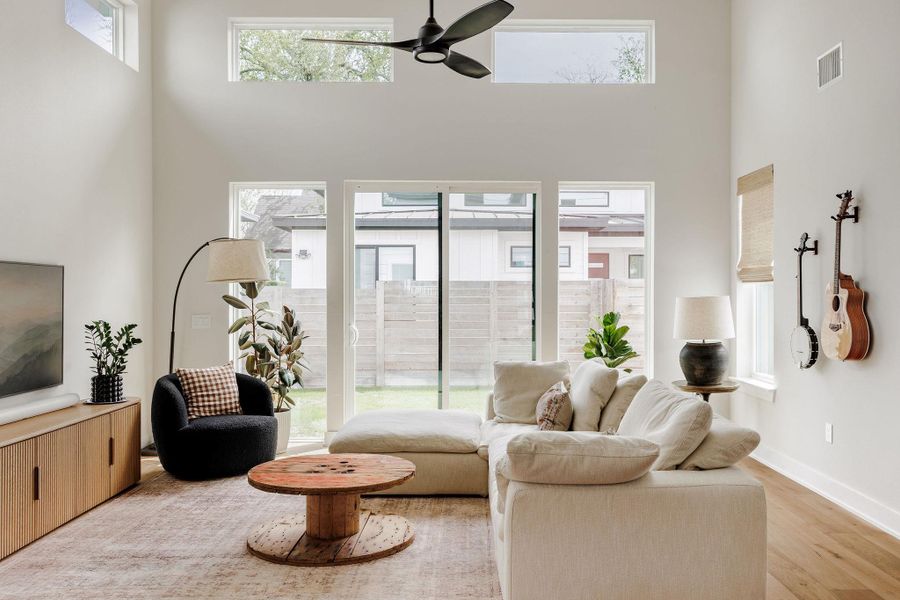 Living area with a ceiling fan, a high ceiling, and light wood finished floors