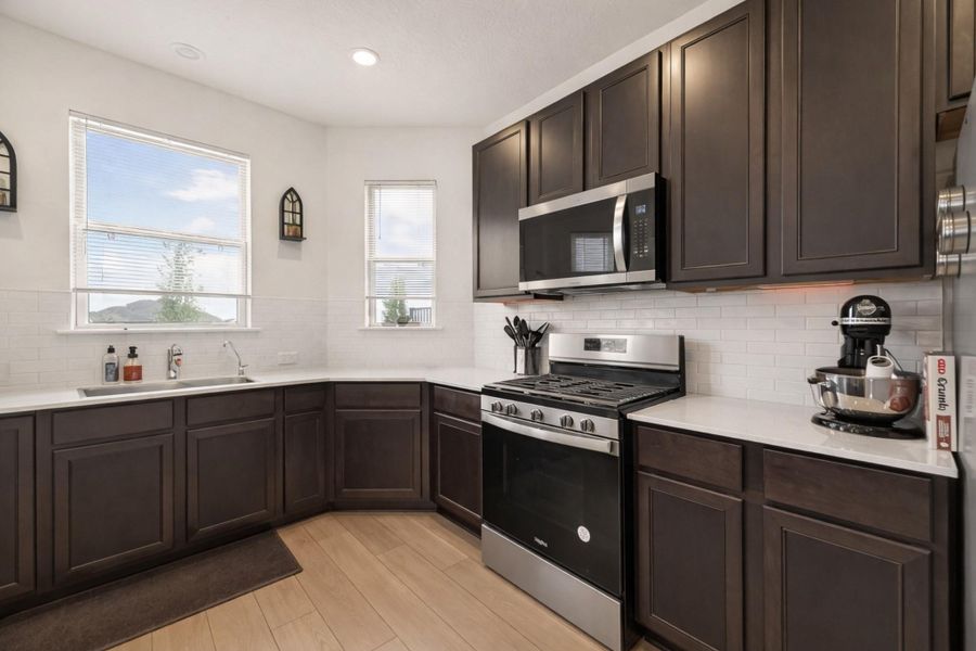Modern U-shaped kitchen with rich cabinetry, bright subway tile backsplash, and expansive quartz-style counters.