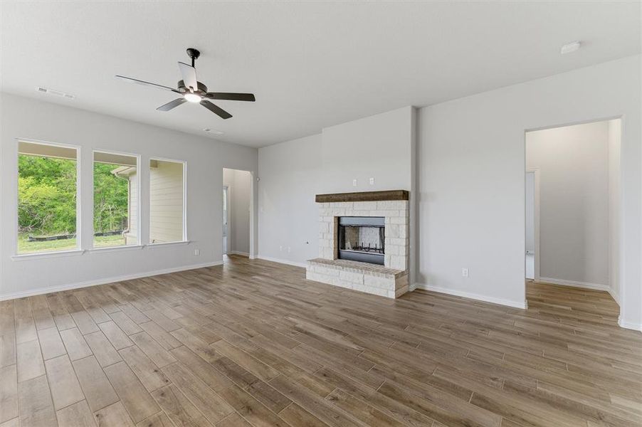 Unfurnished living room with a ceiling fan, light wood-style flooring, and a stone fireplace