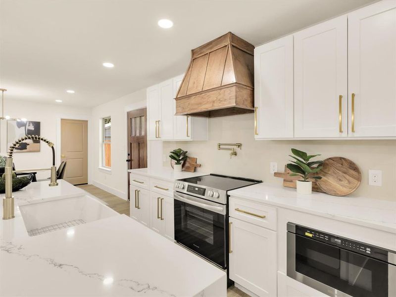 Kitchen with custom exhaust hood, light hardwood / wood-style flooring, sink, appliances with stainless steel finishes, and white cabinets