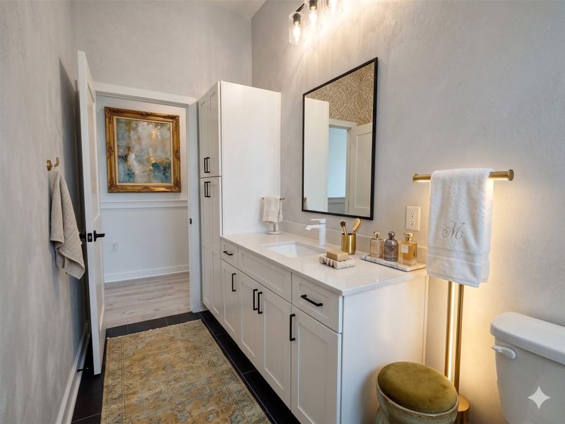 This is a modern bathroom featuring a sleek white vanity with black hardware, a stylish mirror, and elegant lighting. It has a neutral color palette, a decorative rug, and a touch of luxury with gold accents. The space is bright and inviting, ideal for a contemporary home.