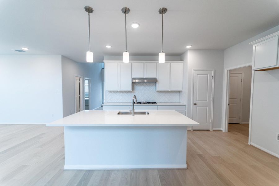 Kitchen with white cabinetry, light wood finished floors, backsplash, and a center island with sink