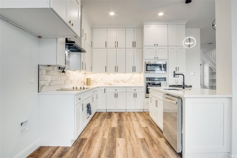 Kitchen with white cabinetry, hanging light fixtures, appliances with stainless steel finishes, light wood-style flooring, and light stone counters