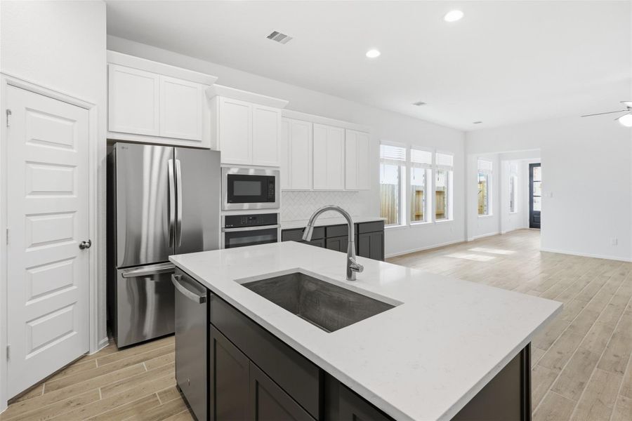 Bright and spacious kitchen with modern stainless steel appliances, sleek white cabinetry, and a large island with a stylish sink, seamlessly flowing into an open living area with abundant natural light.