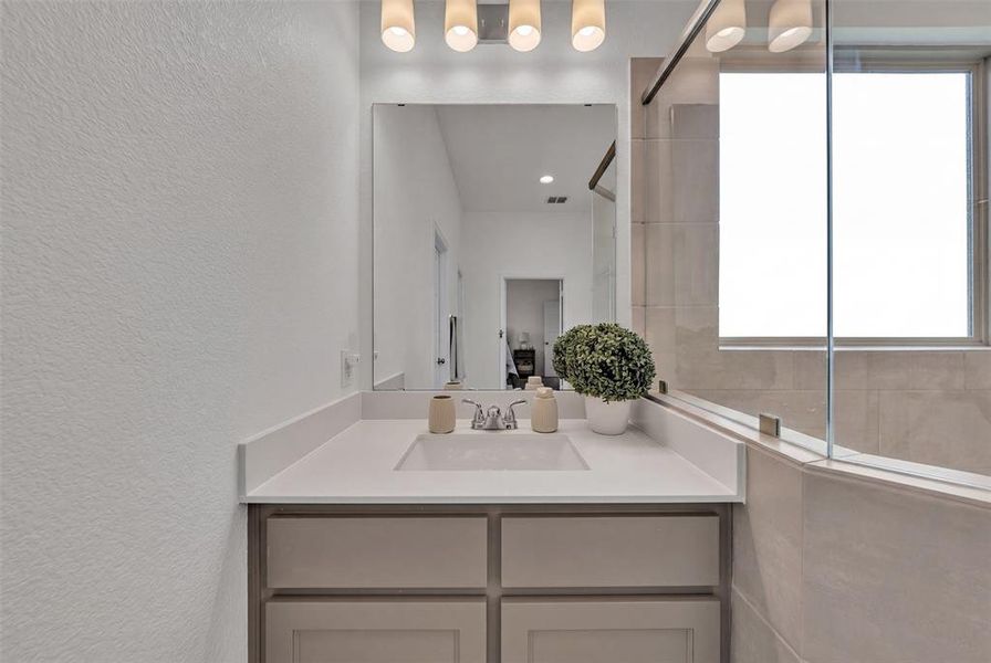 Bathroom vanity featuring a light-toned countertop with an integrated sink, polished chrome faucet, and a large wall-mounted mirror Bathroom vanity featuring a light-toned countertop with an integrated sink, polished chrome faucet, and a large wall-mounted mirror