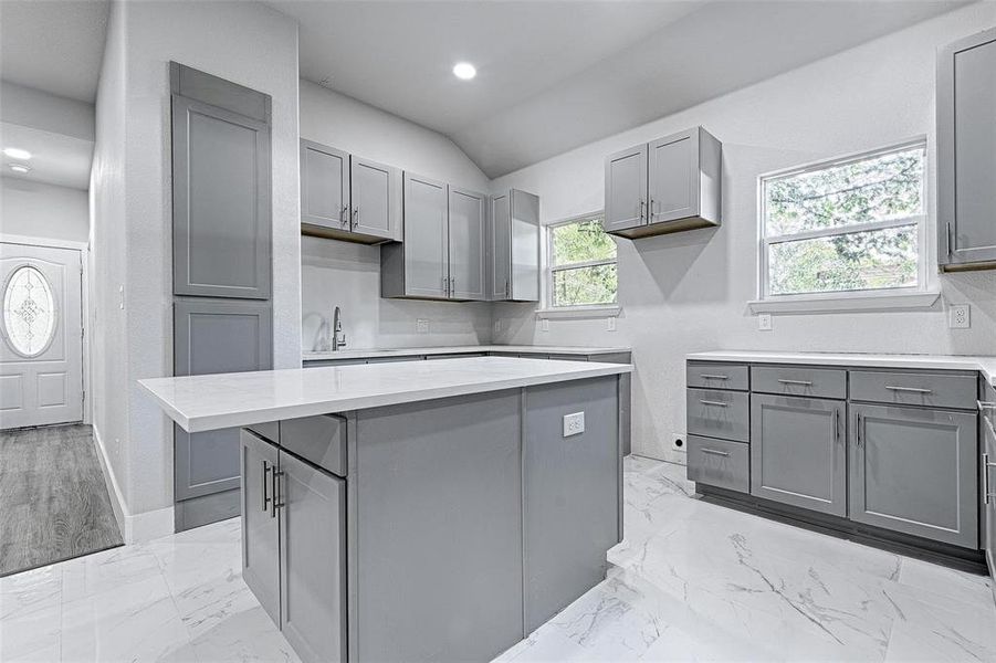 Kitchen with gray cabinets, a kitchen island, lofted ceiling, and decorative backsplash