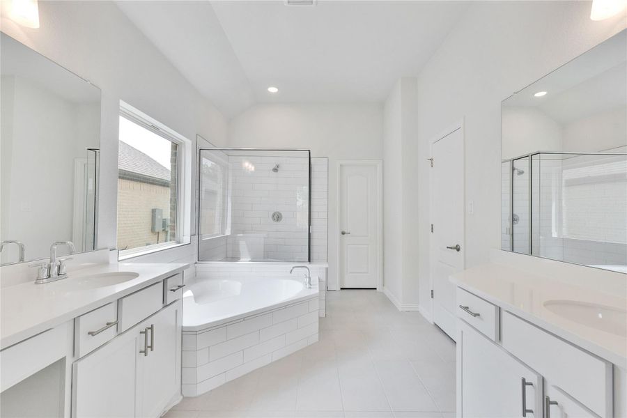 Full bathroom featuring a stall shower, tile patterned flooring, a bath, vaulted ceiling, and two vanities Full bathroom featuring a stall shower, tile patterned flooring, a bath, vaulted ceiling, and two vanities