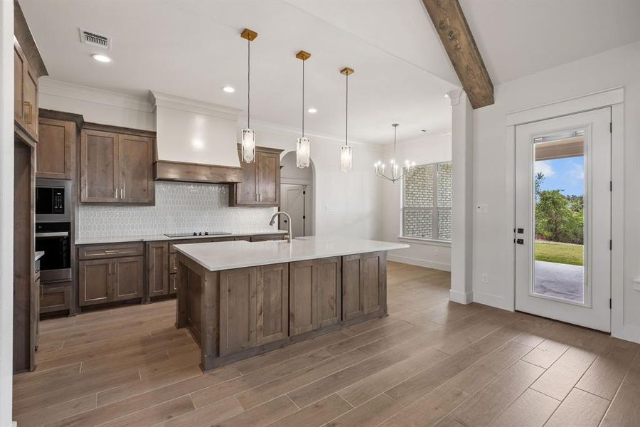 Spacious kitchen featuring an expansive center island with countertop seating, wood-finish cabinetry, built-in stainless steel appliances, and a mosaic tile backsplash