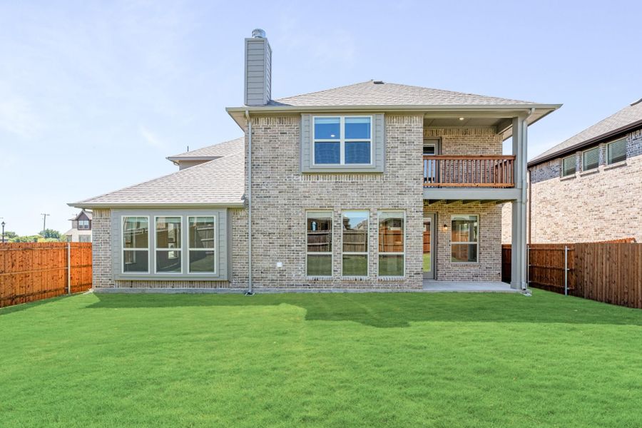 Two-story brick home rear exterior with second-floor balcony, chimney, and fenced backyard with green lawn Two-story brick home rear exterior with second-floor balcony, chimney, and fenced backyard with green lawn