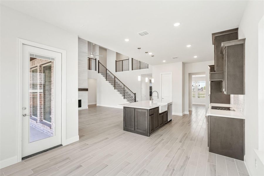 Open-concept kitchen with dark cabinets, white island, and staircase visible in background on light wood-look floors Open-concept kitchen with dark cabinets, white island, and staircase visible in background on light wood-look floors
