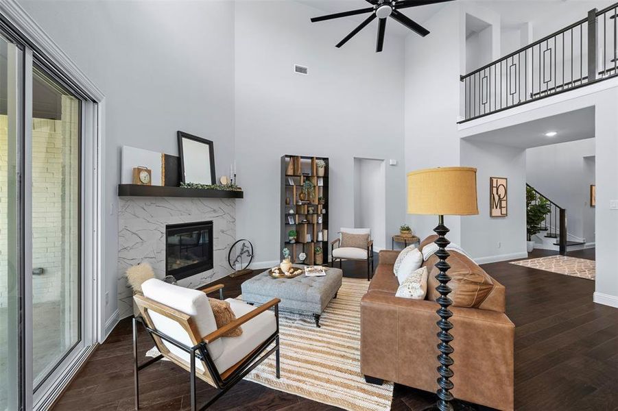 Living room featuring a ceiling fan, wood finished floors, a towering ceiling, a fireplace, and stairs