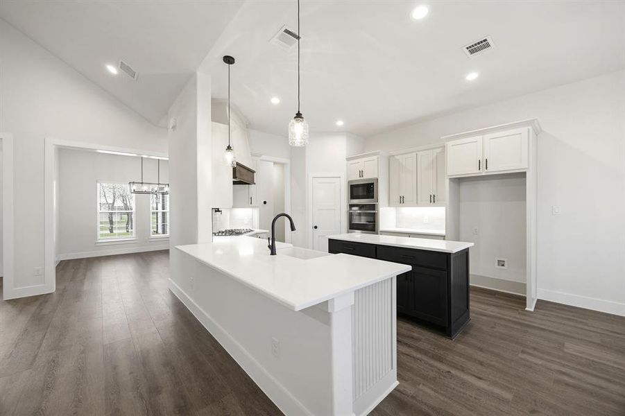 Modern kitchen featuring a large central island with seating, a secondary island with built-in microwave and oven, white cabinetry, dark wood-finish flooring, and recessed lighting