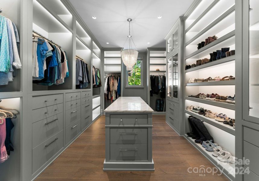 This primary walk-in closet features custom cabinetry and lit shelving.