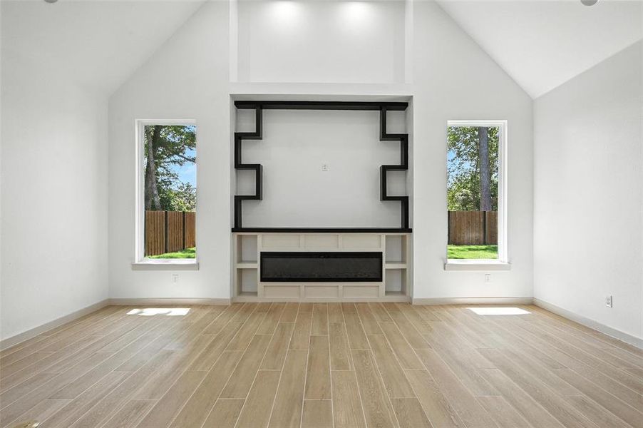 Unfurnished living room featuring wood finished floors, high vaulted ceiling, and plenty of natural light Unfurnished living room featuring wood finished floors, high vaulted ceiling, and plenty of natural light