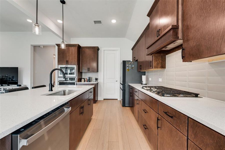 Kitchen with appliances with stainless steel finishes, hanging light fixtures, light wood-style flooring, decorative backsplash, and vaulted ceiling
