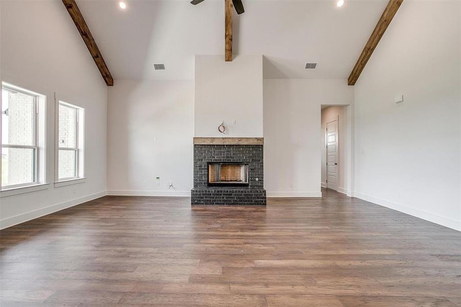 Unfurnished living room with ceiling fan, beamed ceiling, hardwood / wood-style floors, a fireplace, and high vaulted ceiling