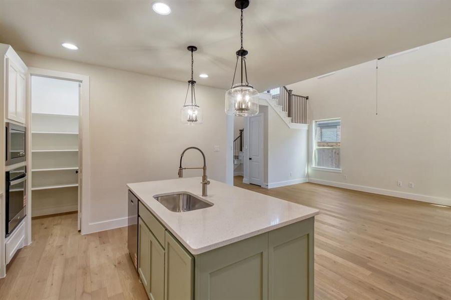 Kitchen with an island with sink, light wood-style floors, open floor plan, light stone countertops, and green cabinetry Kitchen with an island with sink, light wood-style floors, open floor plan, light stone countertops, and green cabinetry