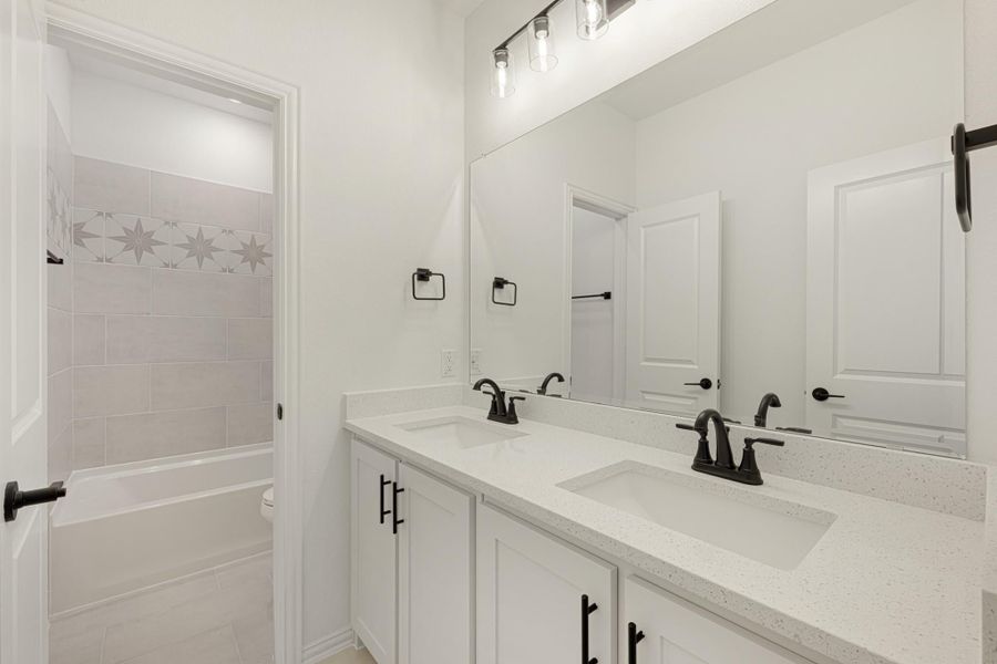 Bathroom with double sink vanity, white quartz countertop, and tiled shower-tub combo with decorative star tile border