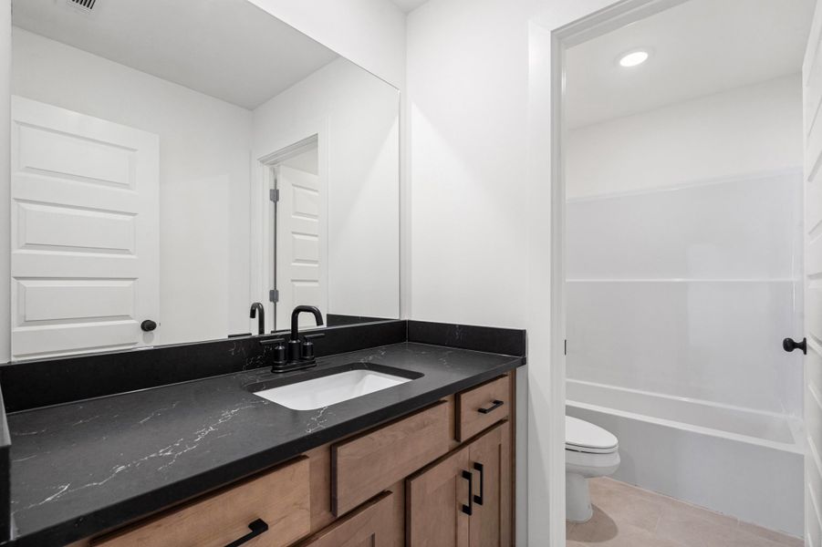 Vanity with wood-finish cabinetry, black countertop, white undermount sink, and matte black faucet