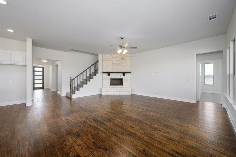 Unfurnished living room featuring ceiling fan, a stone fireplace, and dark wood-type flooring