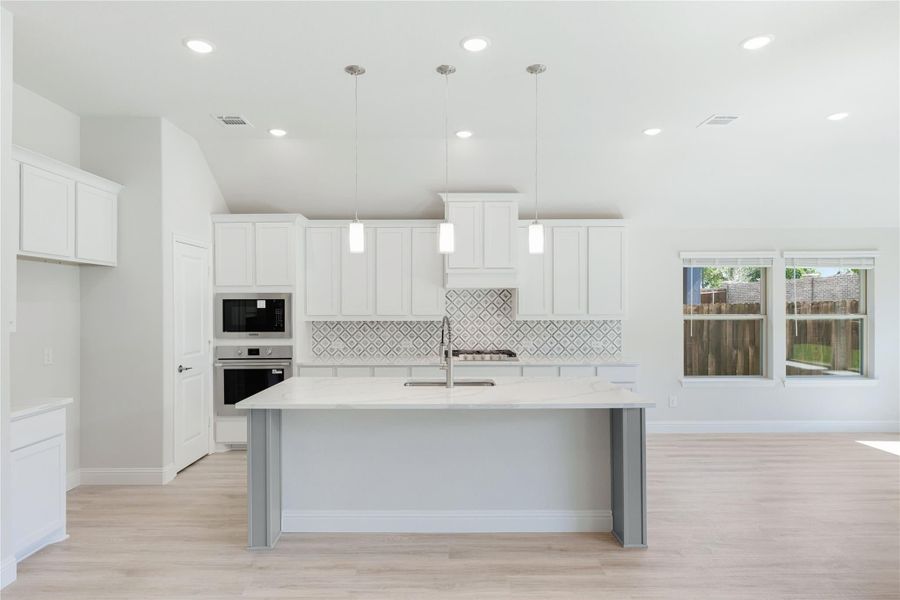 Kitchen with white cabinets, center island, patterned tile backsplash, and stainless steel appliances on light wood floors