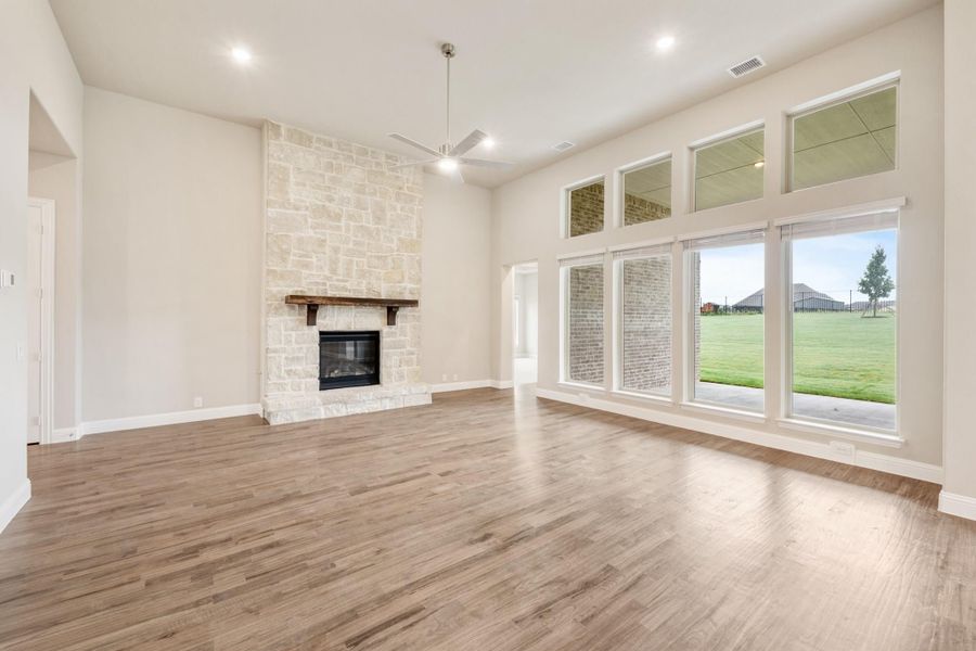 Open living room with stone fireplace, hardwood floors, high ceilings, and large windows overlooking a yard