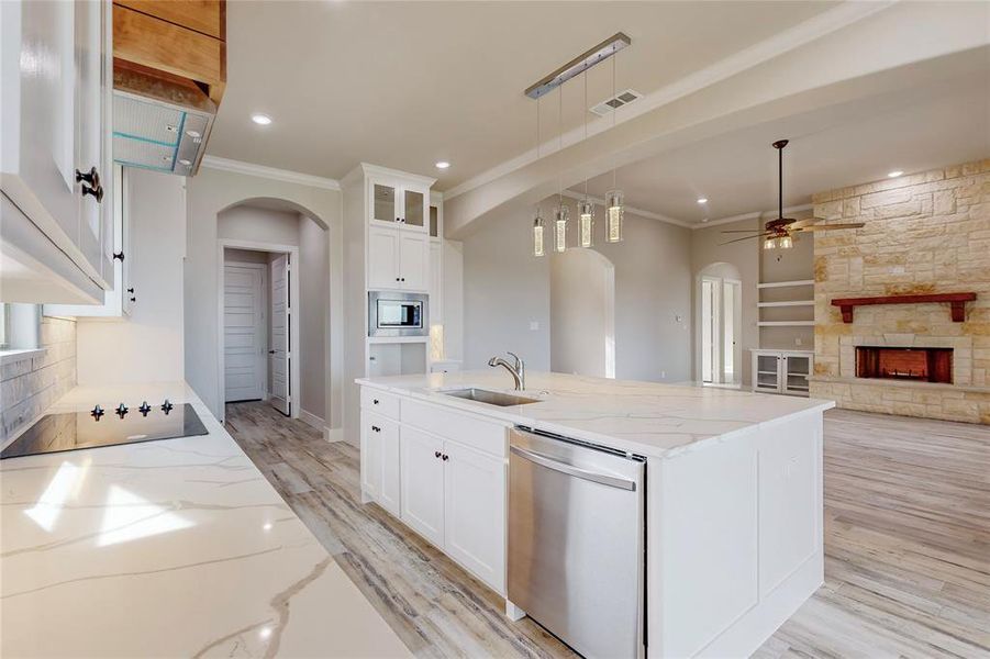 Kitchen with stainless steel appliances, sink, light stone countertops, decorative light fixtures, and white cabinets