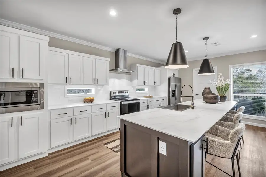 Kitchen featuring white cabinetry, decorative light fixtures, stainless steel appliances, a center island with sink, and a breakfast bar