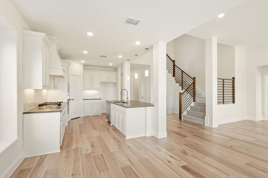 Open kitchen with white cabinets, center island, dark countertops, and light hardwood floors leading to a staircase Open kitchen with white cabinets, center island, dark countertops, and light hardwood floors leading to a staircase