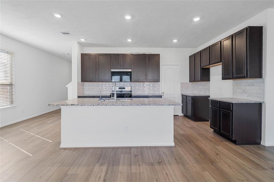 This spacious kitchen features high ceilings, stained wood cabinets, granite countertops, SS appliances, modern tile backsplash, recessed lighting, huge granite kitchen island with sink and space for breakfast bar, and a pantry all overlooking your huge family room.