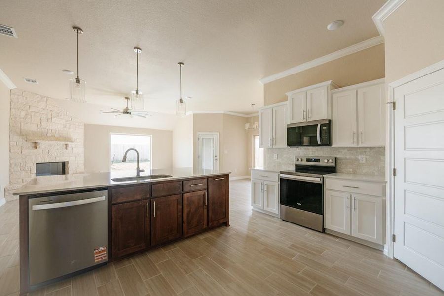 Kitchen with crown molding, appliances with stainless steel finishes, white cabinets, pendant lighting, and open floor plan Kitchen with crown molding, appliances with stainless steel finishes, white cabinets, pendant lighting, and open floor plan