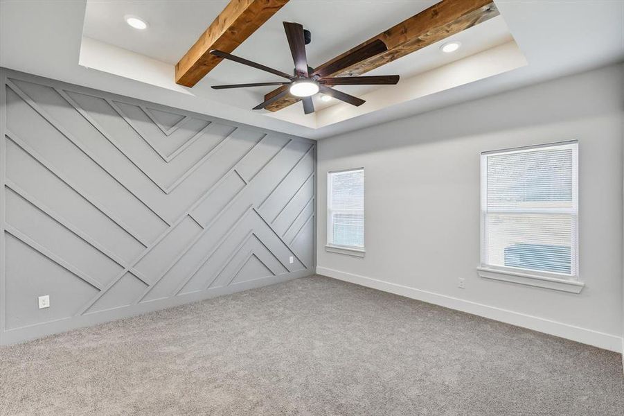 Empty room with beamed ceiling, healthy amount of natural light, light carpet, and a ceiling fan