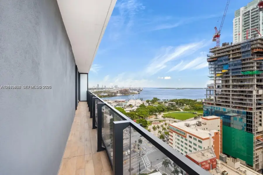 Covered balcony featuring wood-finish flooring, solid partition walls, and a glass-panel railing Covered balcony featuring wood-finish flooring, solid partition walls, and a glass-panel railing