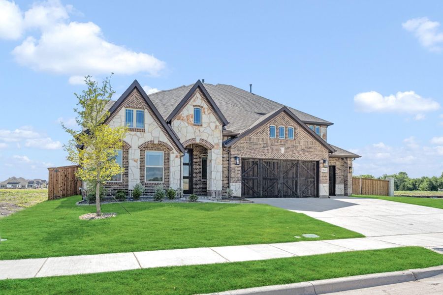 Two-story home with brick and stone exterior, three-car garage with wood doors, and green front lawn Two-story home with brick and stone exterior, three-car garage with wood doors, and green front lawn
