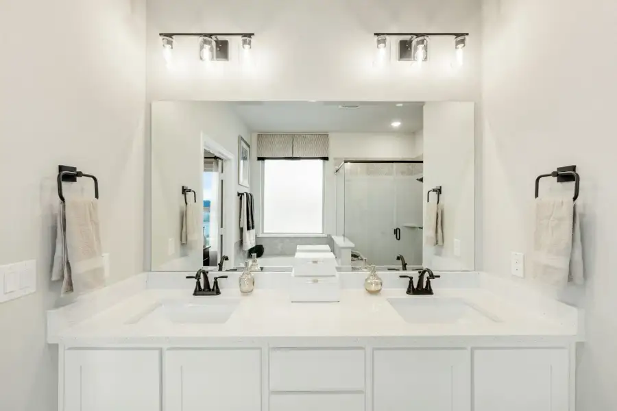 Bathroom with double sink vanity, white cabinets, large mirror, and walk-in shower visible in reflection