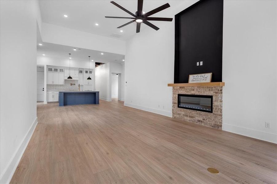Unfurnished living room featuring light wood-style flooring, a glass covered fireplace, ceiling fan, and recessed lighting