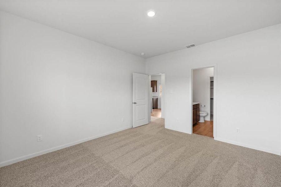 Bedroom with connected bathroom, light colored carpet, and recessed lighting