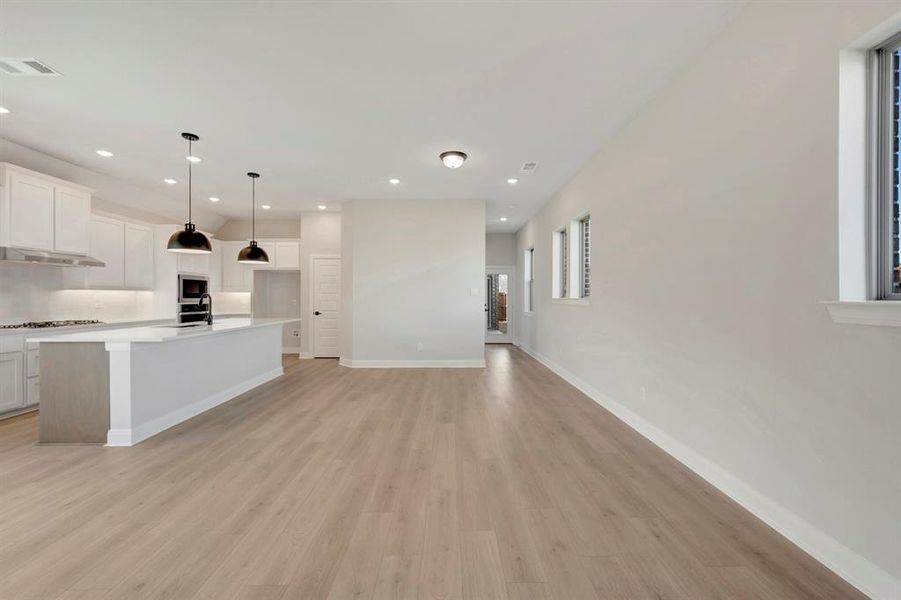Kitchen with white cabinets, light wood-style flooring, a center island with sink, open floor plan, and decorative light fixtures