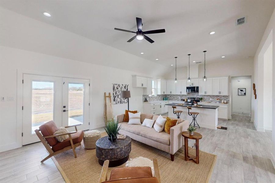 Living room featuring ceiling fan, french doors, light hardwood / wood-style flooring, and vaulted ceiling