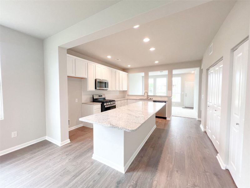 Kitchen featuring white cabinets, stainless steel appliances, a center island, light wood finished floors, and light stone counters