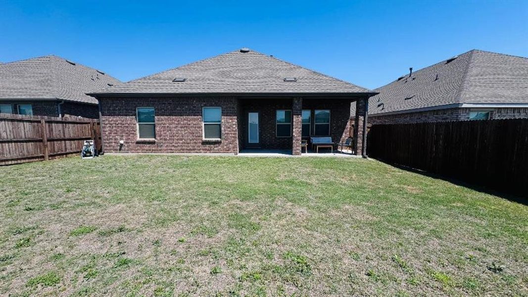 Rear view of property featuring brick siding, a fenced backyard, a yard, and a patio area