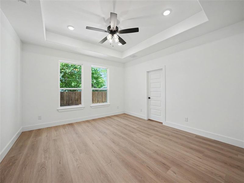 Spacious room featuring wood-finish flooring, a tray ceiling with recessed lighting and a ceiling fan, and two large windows offering natural light Spacious room featuring wood-finish flooring, a tray ceiling with recessed lighting and a ceiling fan, and two large windows offering natural light