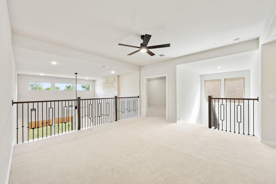 Open upstairs loft with carpet flooring, black ceiling fan, and iron stair railings on both sides