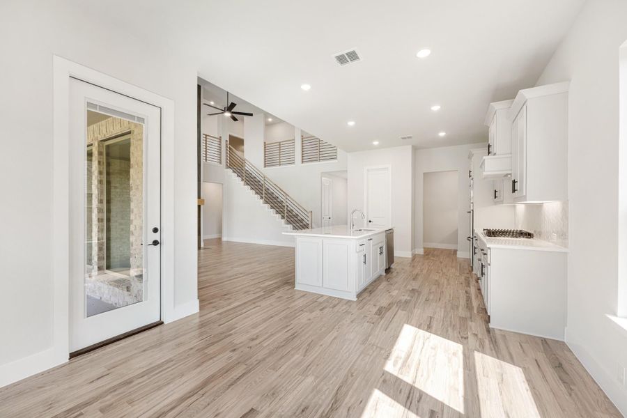 Open-concept kitchen with white island, light wood floors, and staircase visible in background