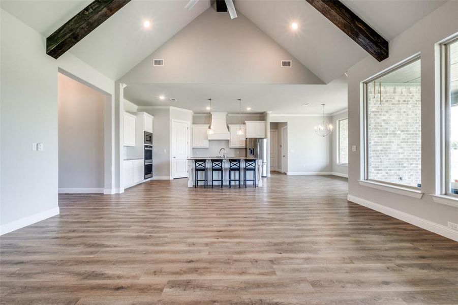 Unfurnished living room with beamed ceiling, light hardwood / wood-style flooring, sink, high vaulted ceiling, and a notable chandelier