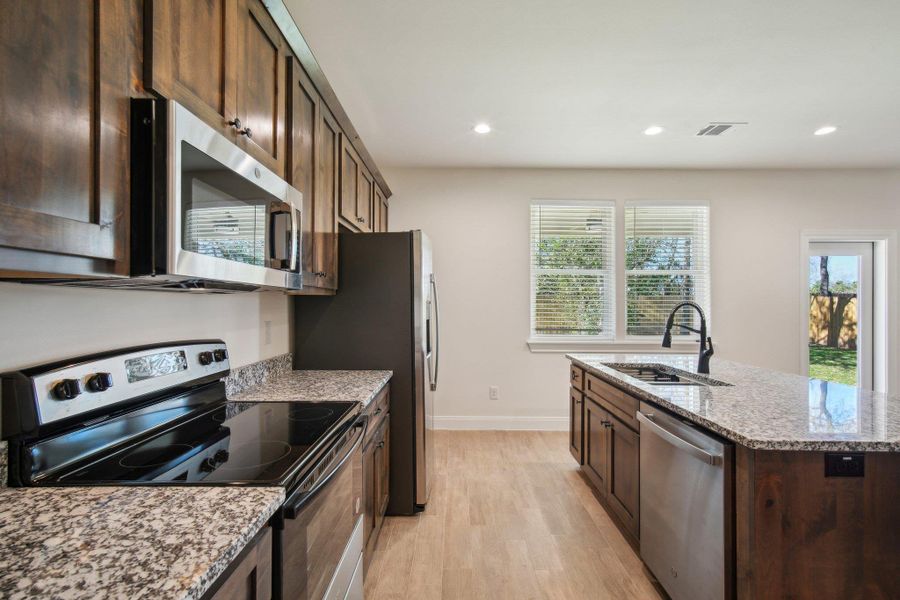 Kitchen featuring visible vents, light stone countertops, a kitchen island with sink, stainless steel appliances, and a sink Kitchen featuring visible vents, light stone countertops, a kitchen island with sink, stainless steel appliances, and a sink